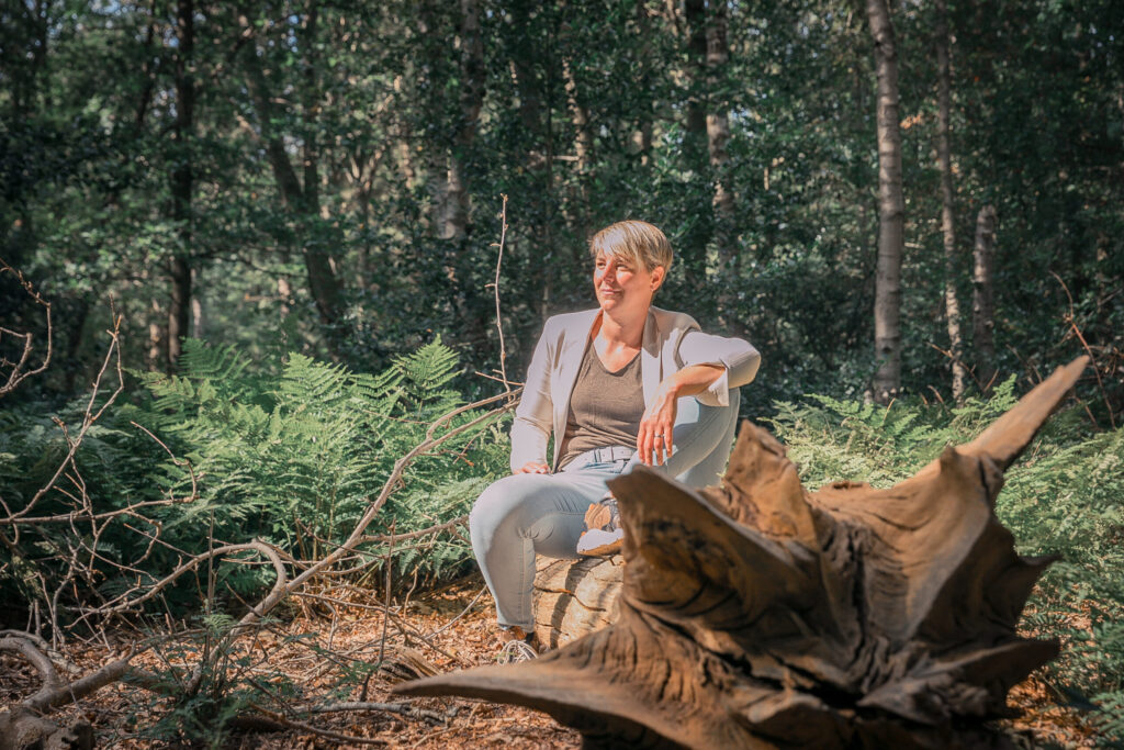 Ellen Baas zittend op boomstam in zonnig bos